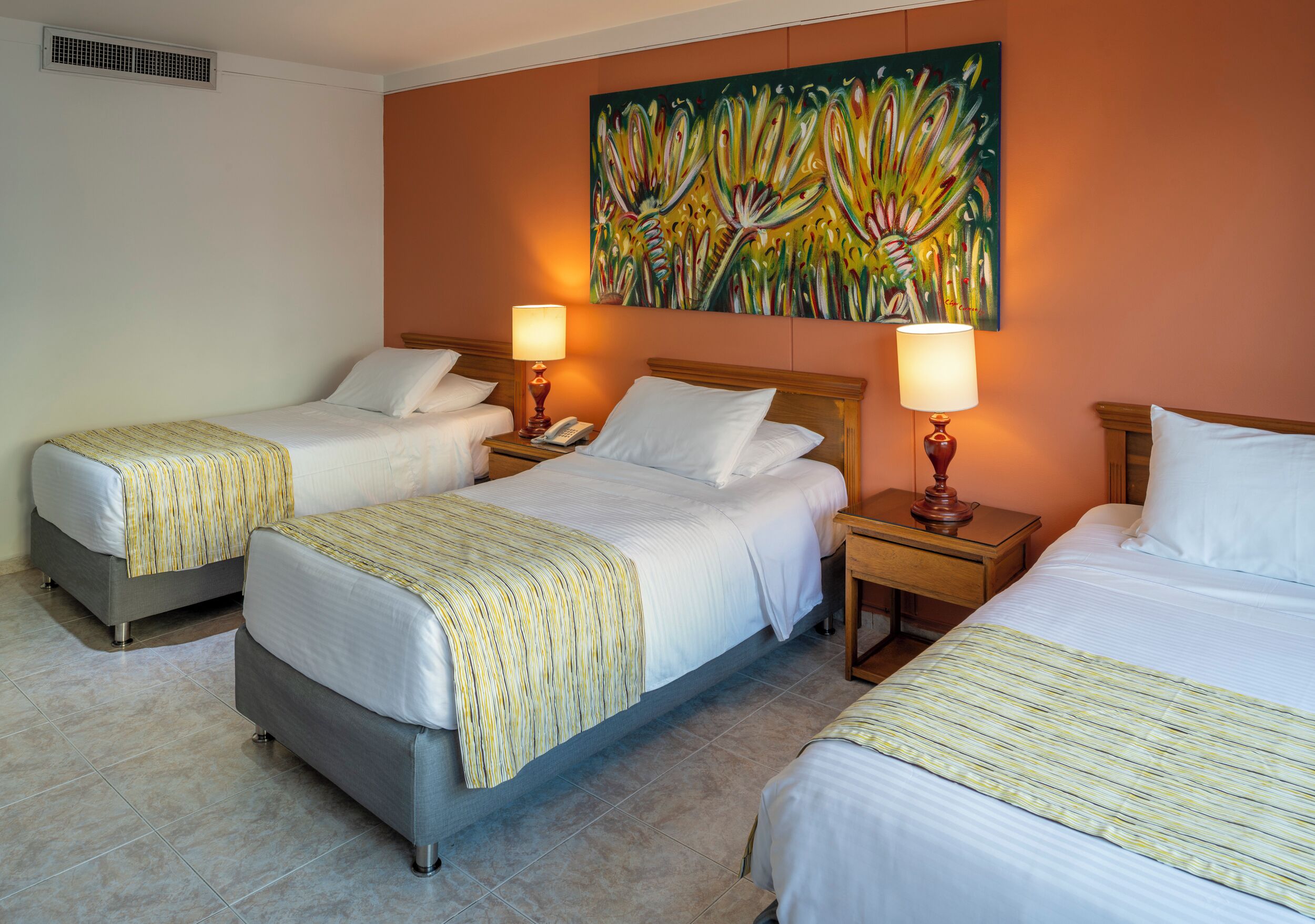 A hotel room with two single beds, a double bed, and a painting on the wall.