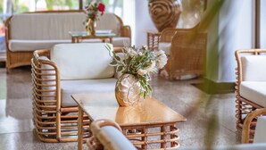 A modern interior with wicker furniture, a wooden table with a vase, and large windows offering a view of greenery outside. - Hotel Arena Blanca (San Andrés)