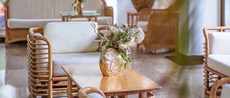 Ein modernes Interieur mit Korbmöbeln, einem Holztisch mit einer Vase und großen Fenstern mit Blick auf die grüne Umgebung.