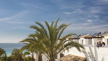 A coastal property with a view of the sea, palm trees, and a building with a tiled roof.