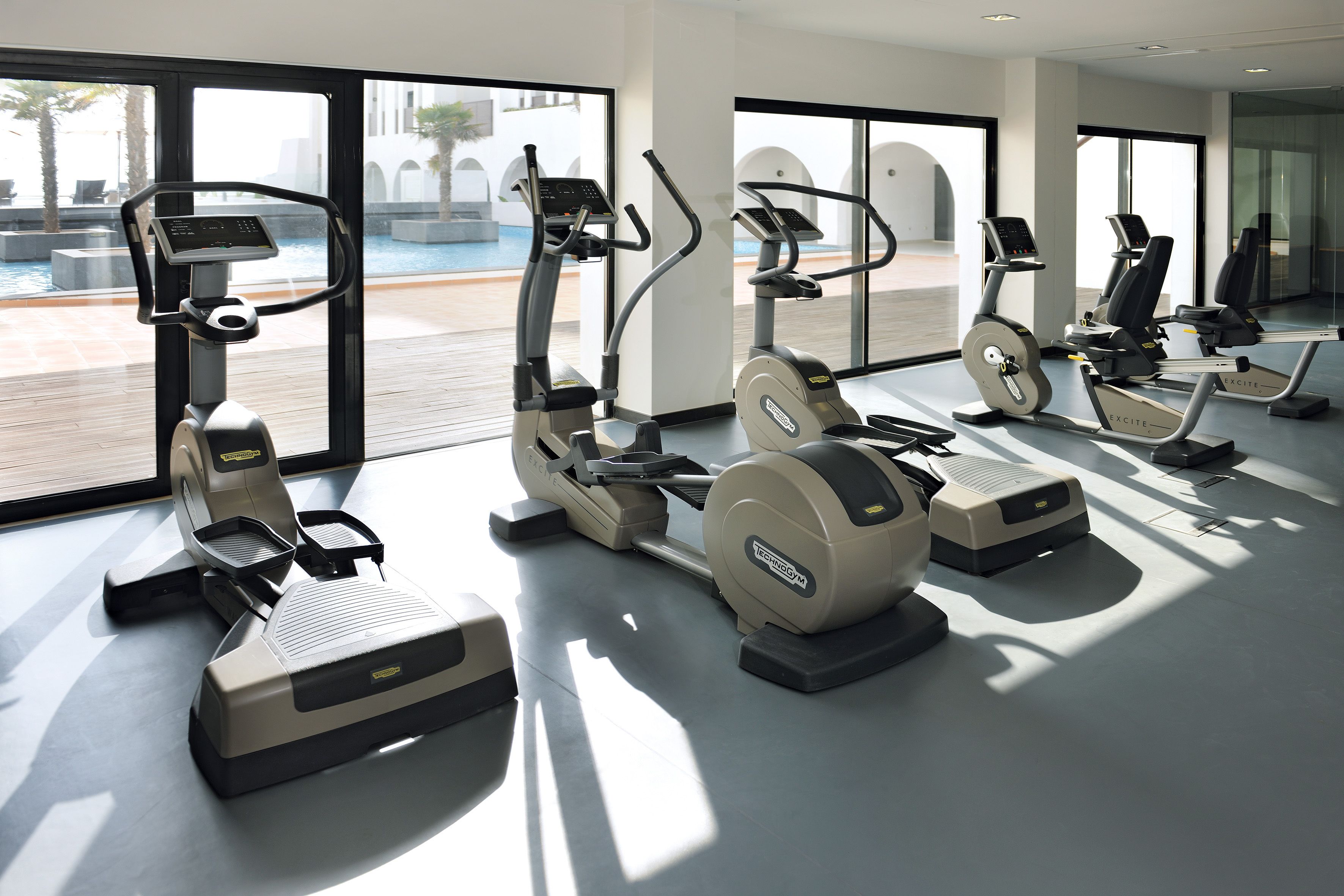 Una palestra con cyclette e tapis roulant, ampie finestre e vista sulla piscina.