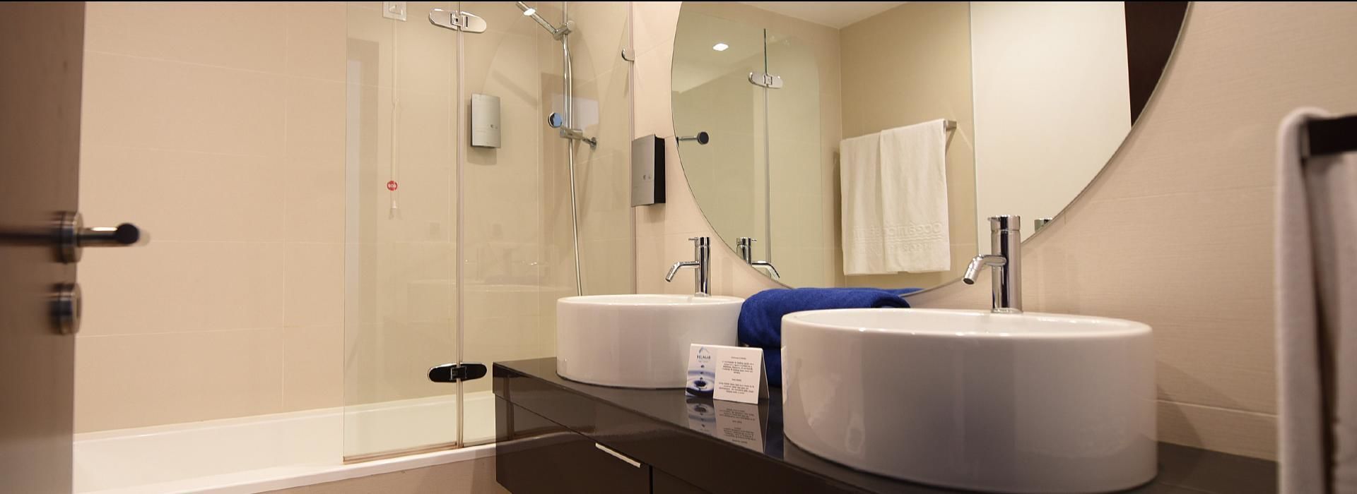 Un baño moderno con ducha envuelta en vidrio, dos lavamanos y un espejo grande.
