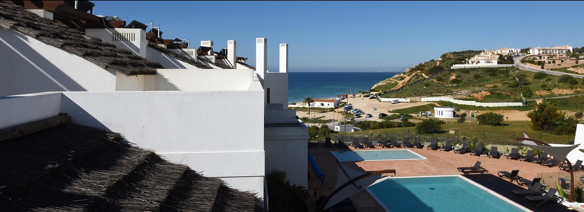A hotel with a rooftop pool, a view of the sea, and a hillside with buildings.
