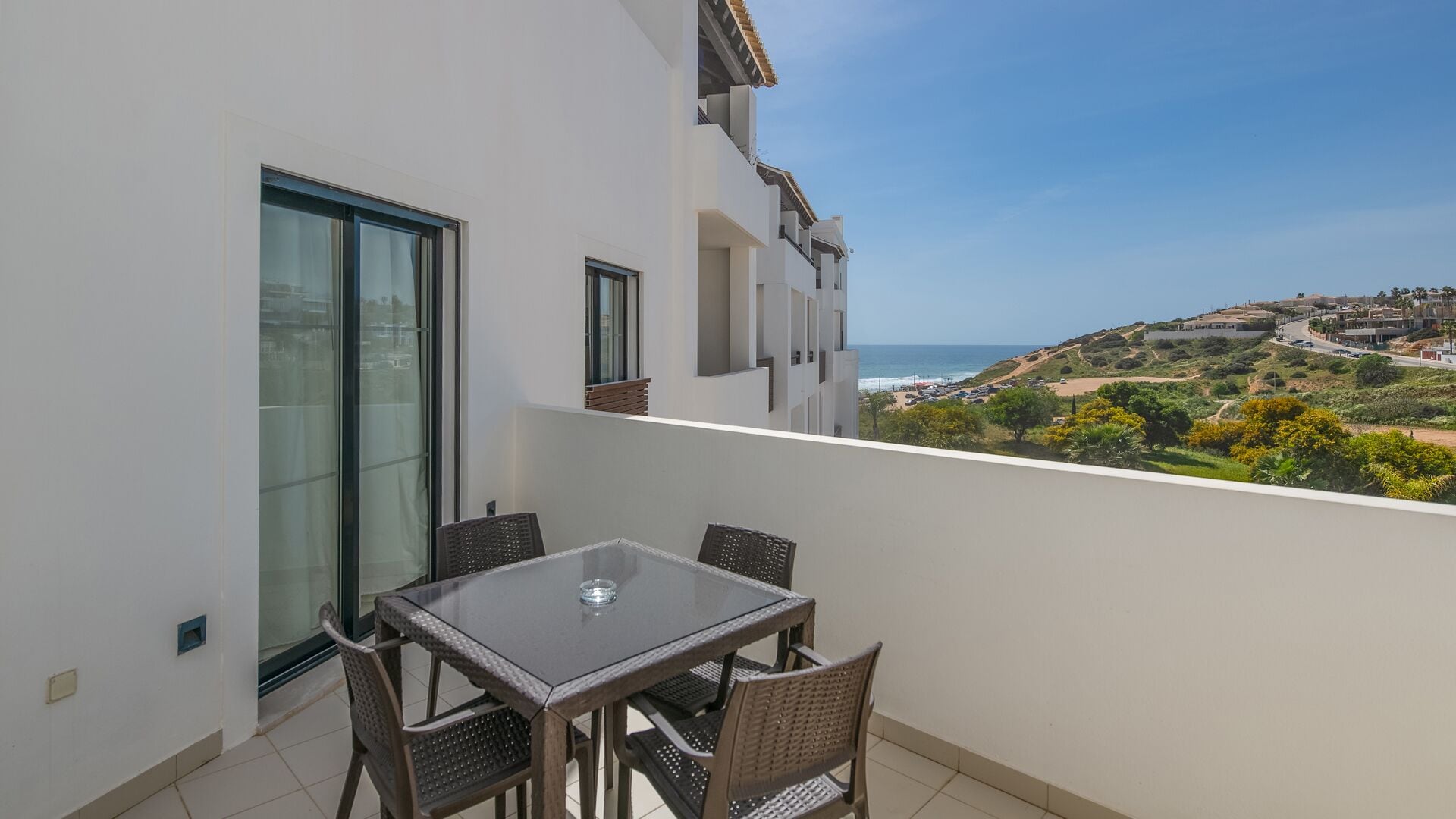 Un balcon avec une table et des chaises, donnant sur un paysage côtier avec des bâtiments et une plage.