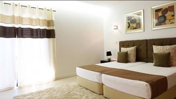 Quarto com cama de casal, duas mesas de cabeceira, uma cadeira e uma janela grande com cortinas.