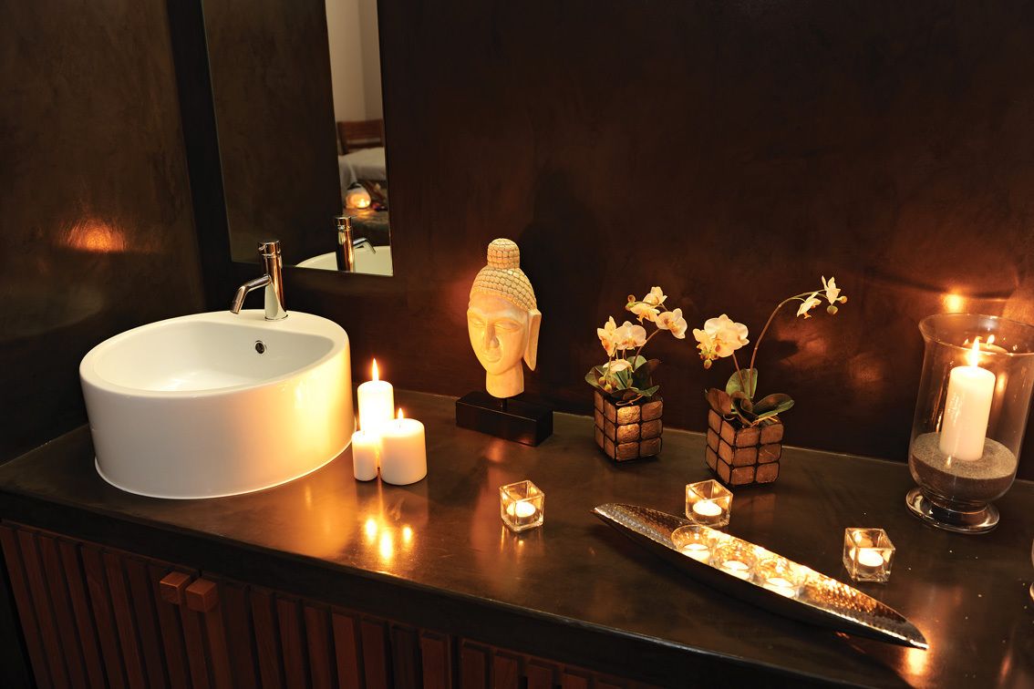 A bathroom vanity with a white sink, multiple candles, a Buddha statue, and small potted plants.