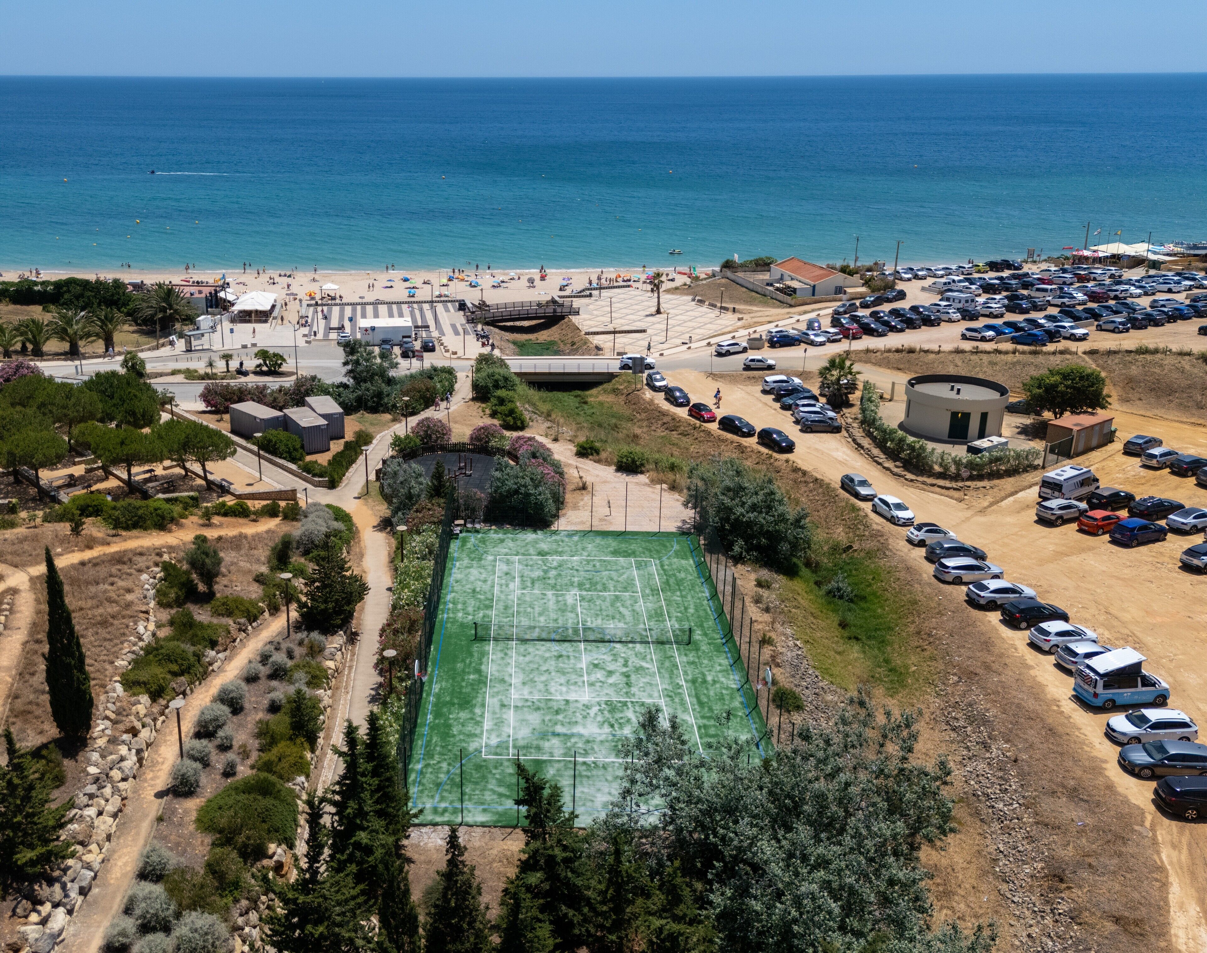 An aerial view of a coastal area with a tennis court, parking lot, and beach.