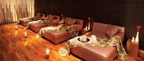 A spa room with multiple massage tables, each with a candle and a tray of amenities.