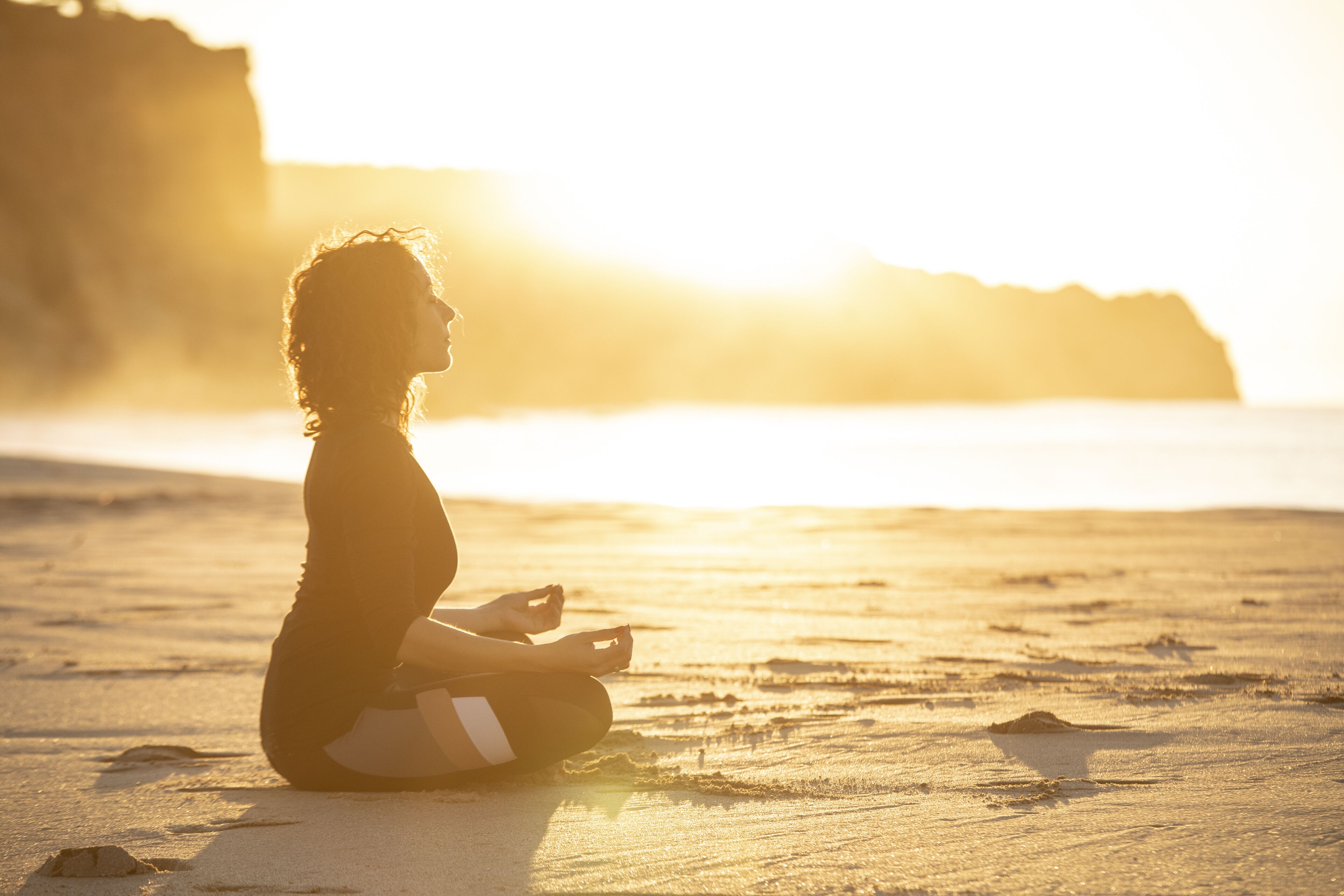 A person sitting on a sandy beach with a cliff in the background.