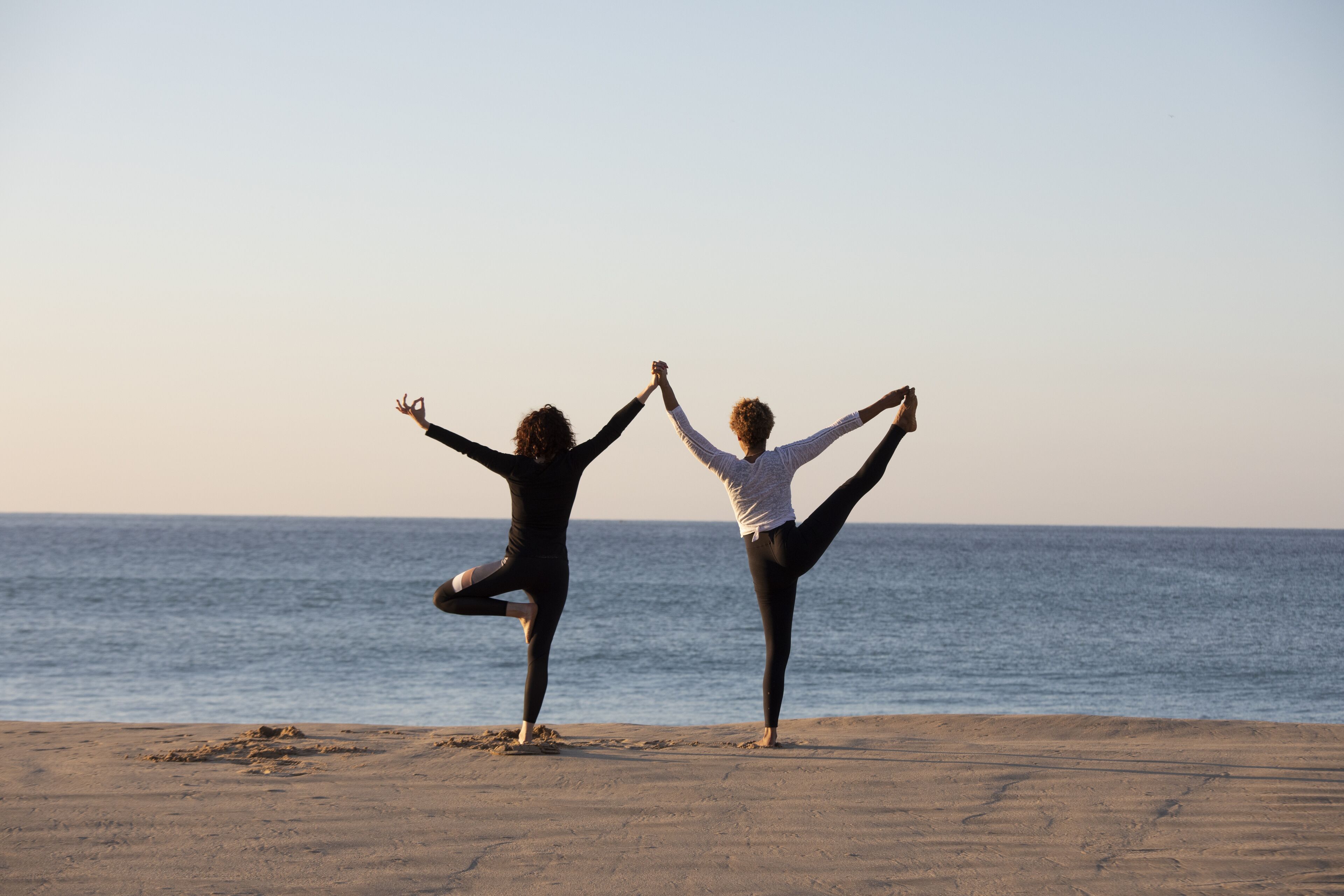 Two people performing yoga on a beach with the ocean in the background.