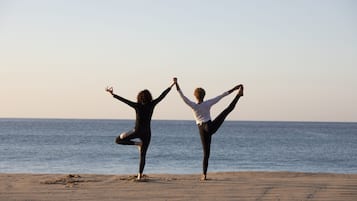 Dos personas practicando yoga en una playa, con el océano al fondo.