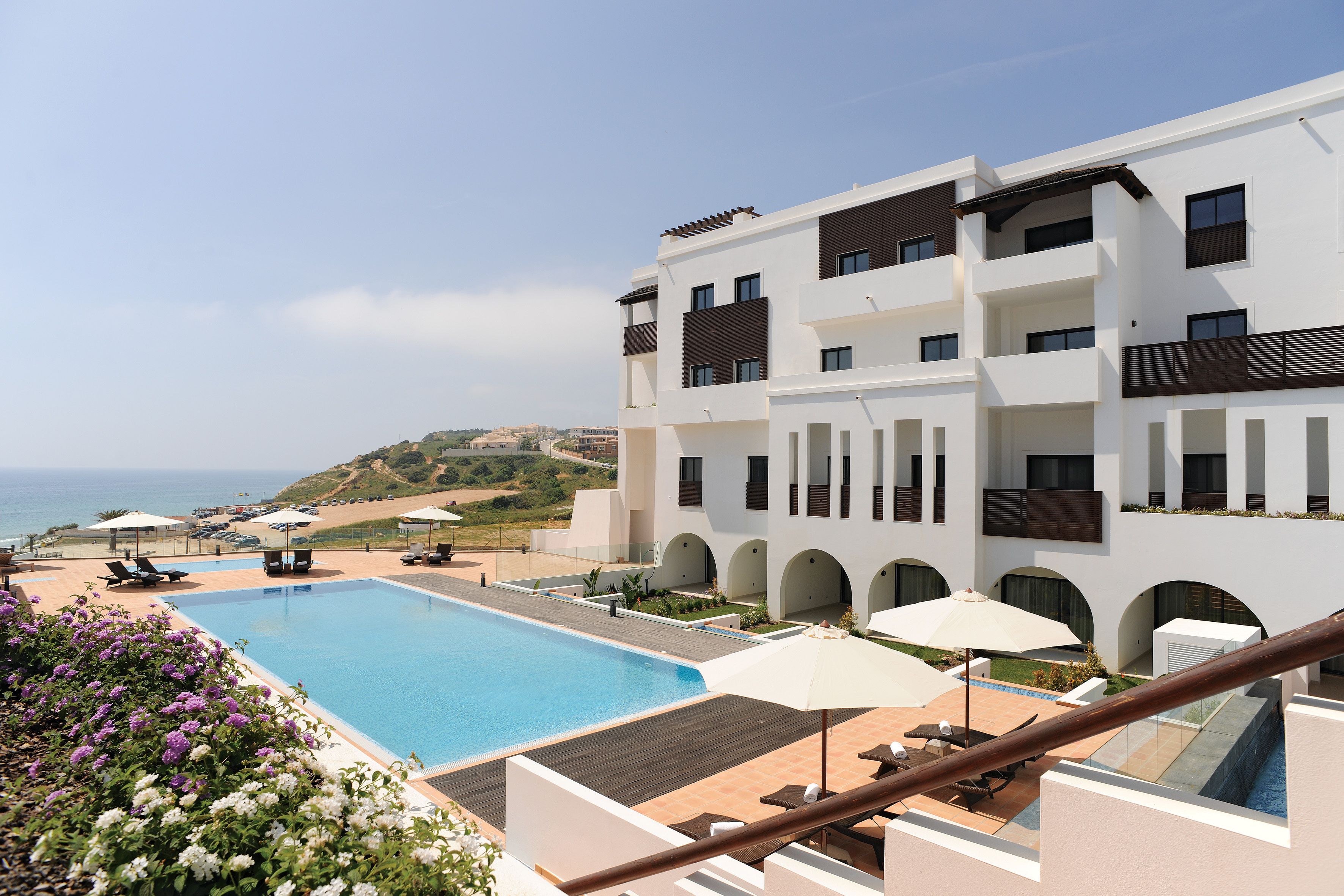 A modern hotel with a swimming pool, outdoor seating, and a view of the sea.