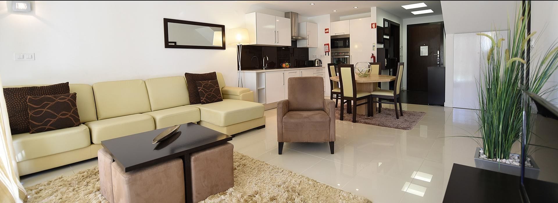 A modern living room with a sofa, a small table, and a chair. There is a kitchen area in the background with cabinets and a dining table.