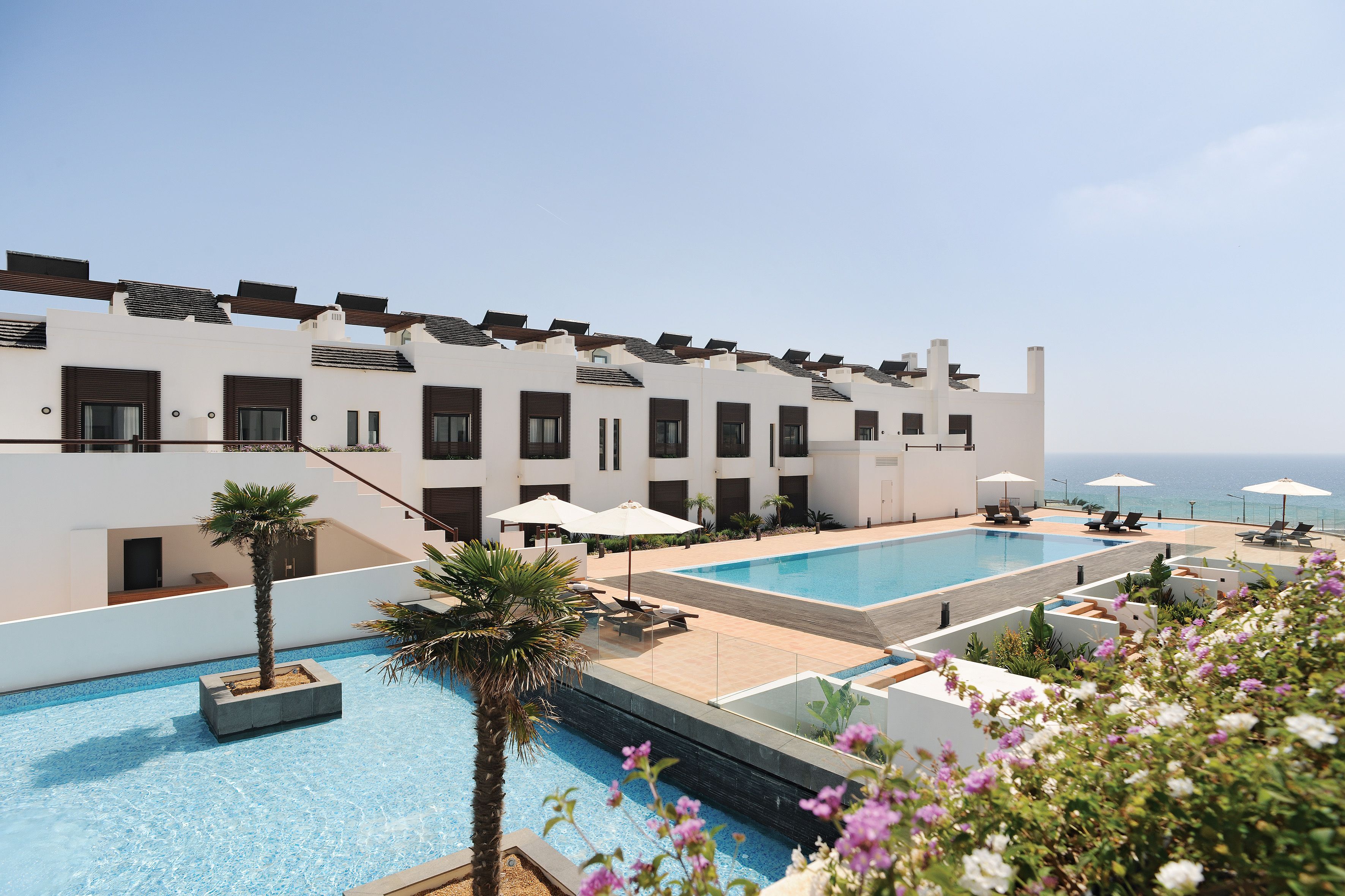 A modern hotel with a rooftop pool, sun loungers, and a view of the sea.