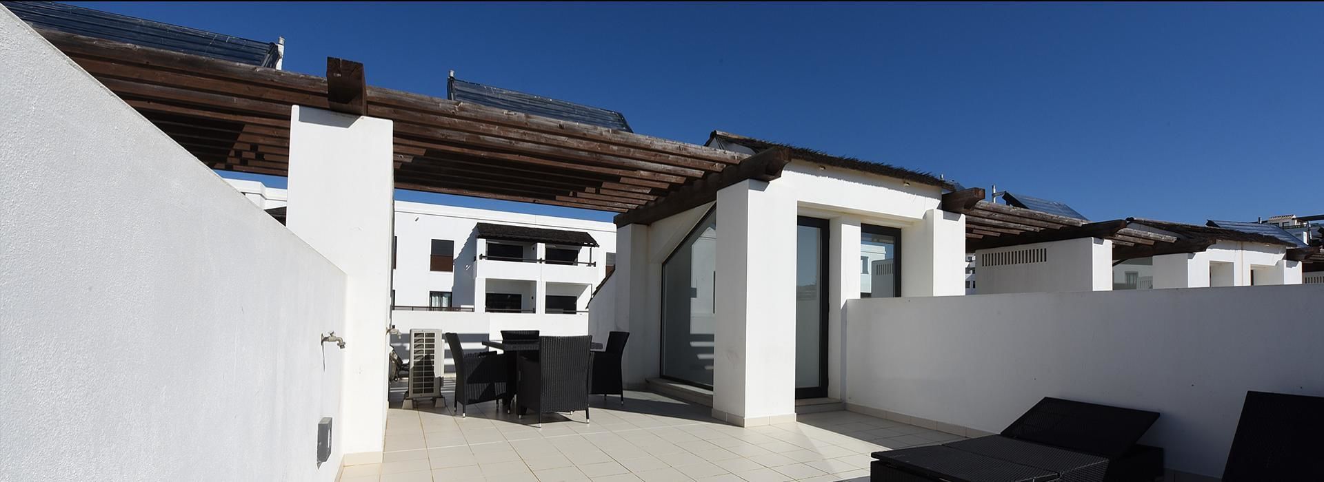 Ein moderner Außenbereich mit Terrasse, einer Pergola, einer Schiebetür zu einem Balkon und einer Sitzecke mit Tisch und Stühlen.