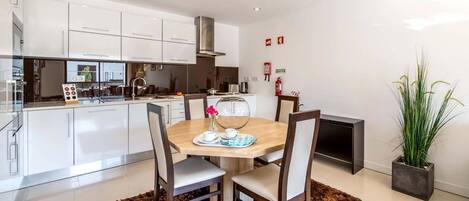 A modern kitchen with white cabinets, a wooden dining table with chairs, and a potted plant.