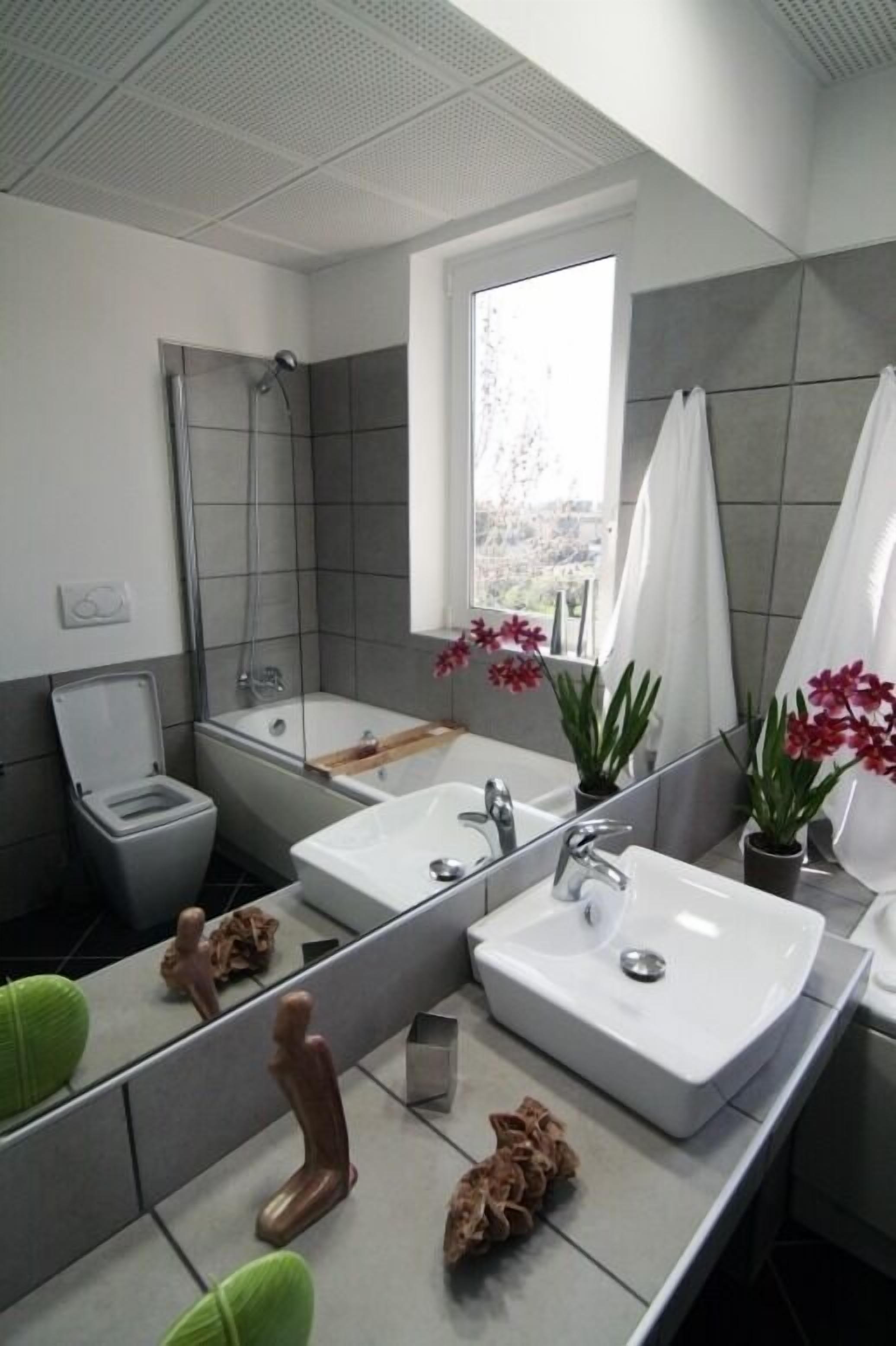 A modern bathroom with a large mirror, two sinks, a shower, and a toilet.