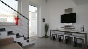 Una sala de estar moderna con una escalera, un televisor de pantalla plana y un diseño minimalista.