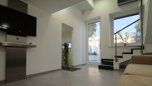 Una sala de estar moderna con televisor de pantalla plana, cocina integrada, escalera y un amplio ventanal.