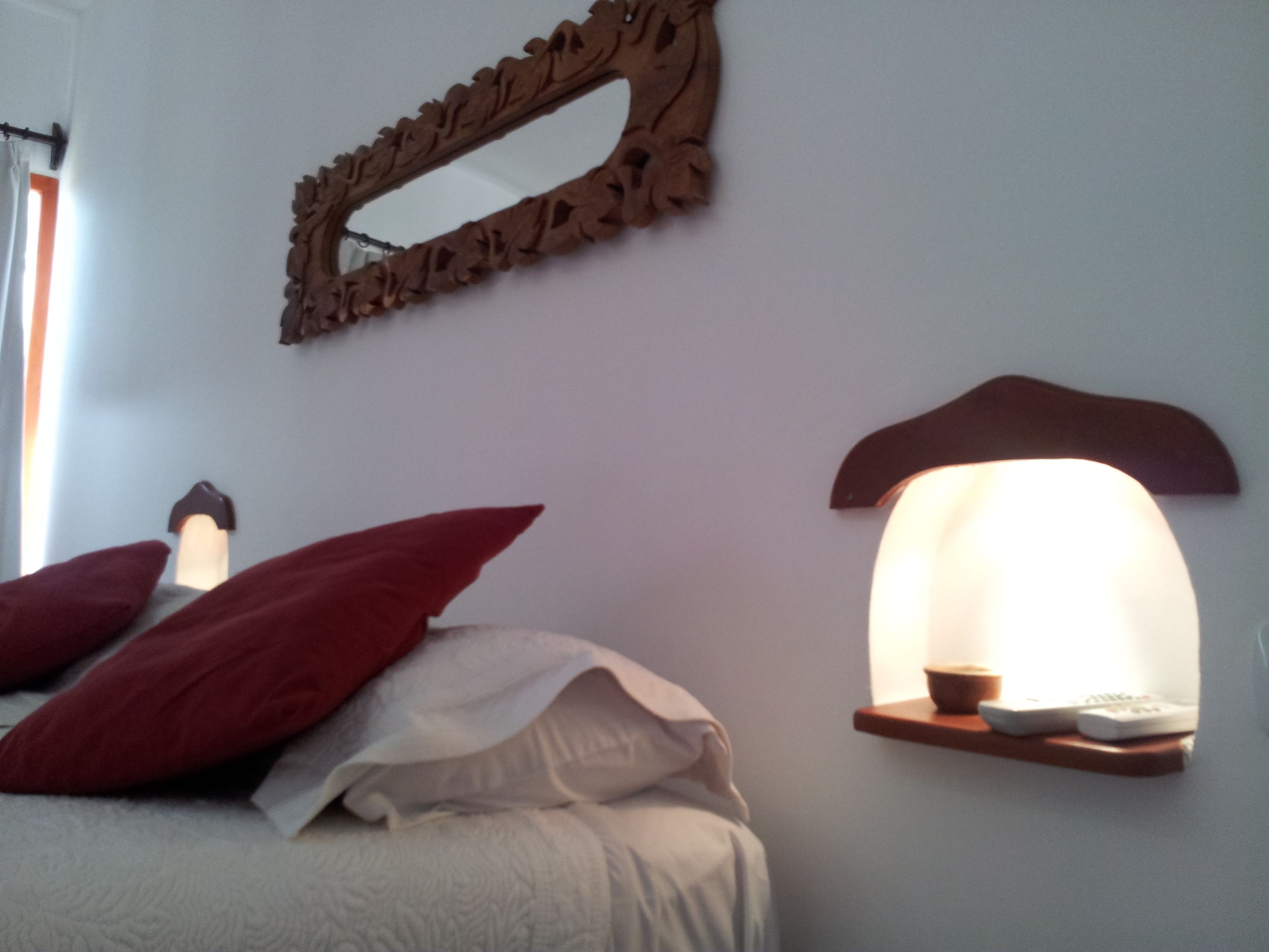 A bed with red and white pillows, a wall-mounted mirror, and a wall-mounted reading light.
