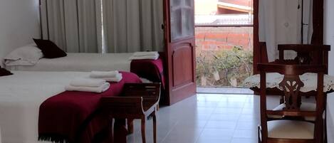 A hotel room with two beds, a chandelier, an air conditioner, a dining table with chairs, and a view of the outside.