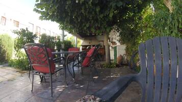 An outdoor patio with metal chairs and a table, surrounded by greenery and a tiled floor.