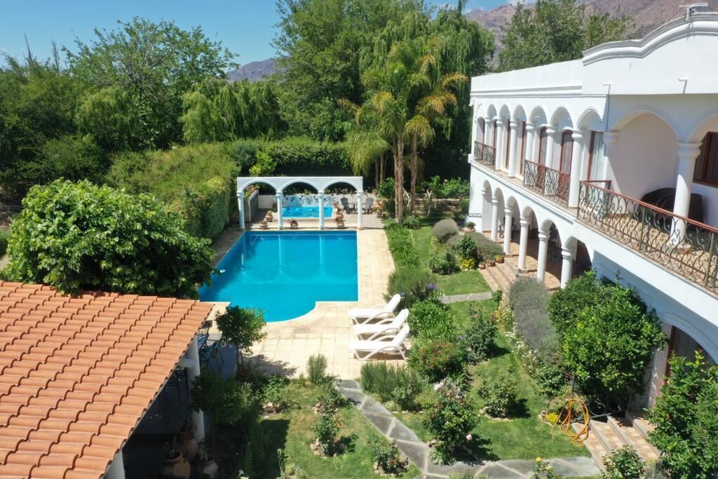 A pool surrounded by lush greenery and a white building with arches.