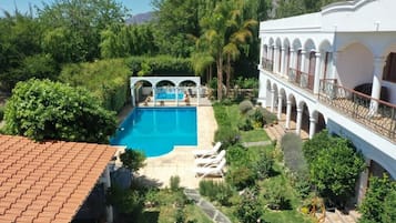 A pool surrounded by lush greenery and a white building with arches.