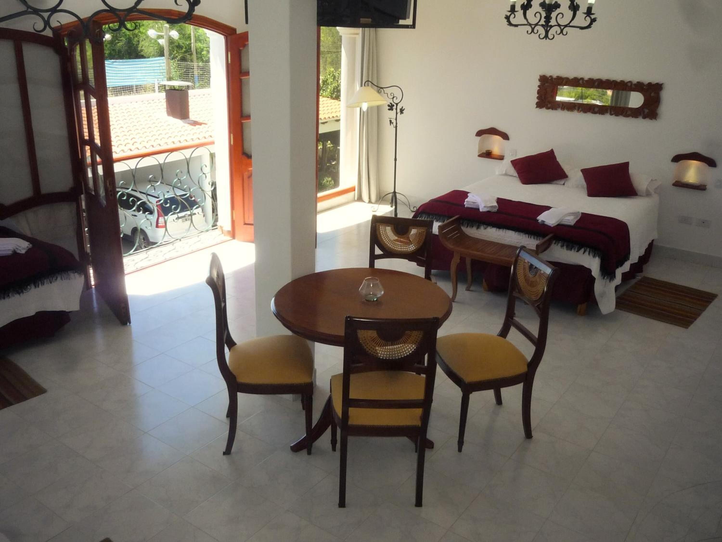 A cozy room with a bed, a dining table with chairs, and a balcony with a view of the street.
