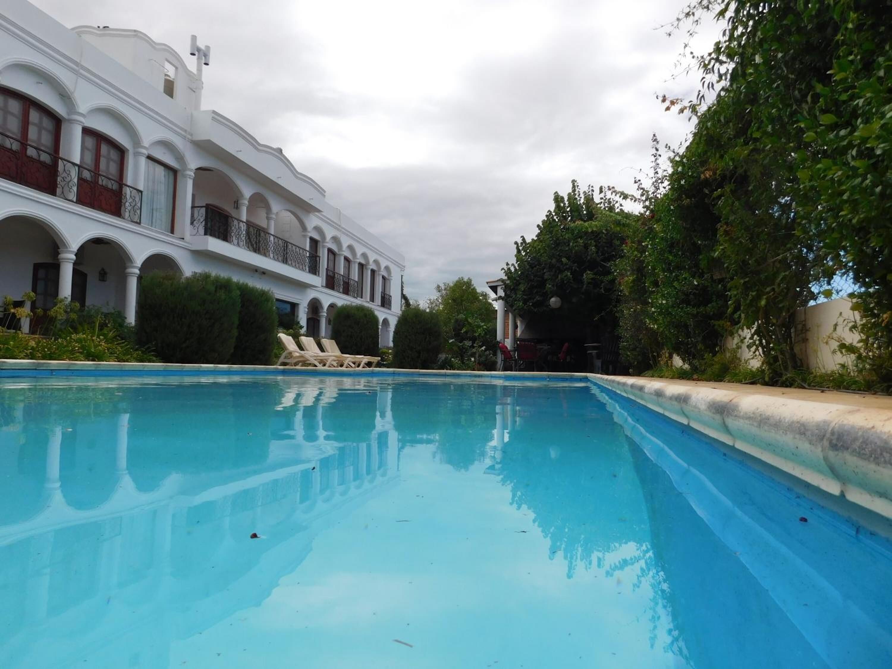 A swimming pool with lounge chairs, surrounded by a white building with arches and balconies.