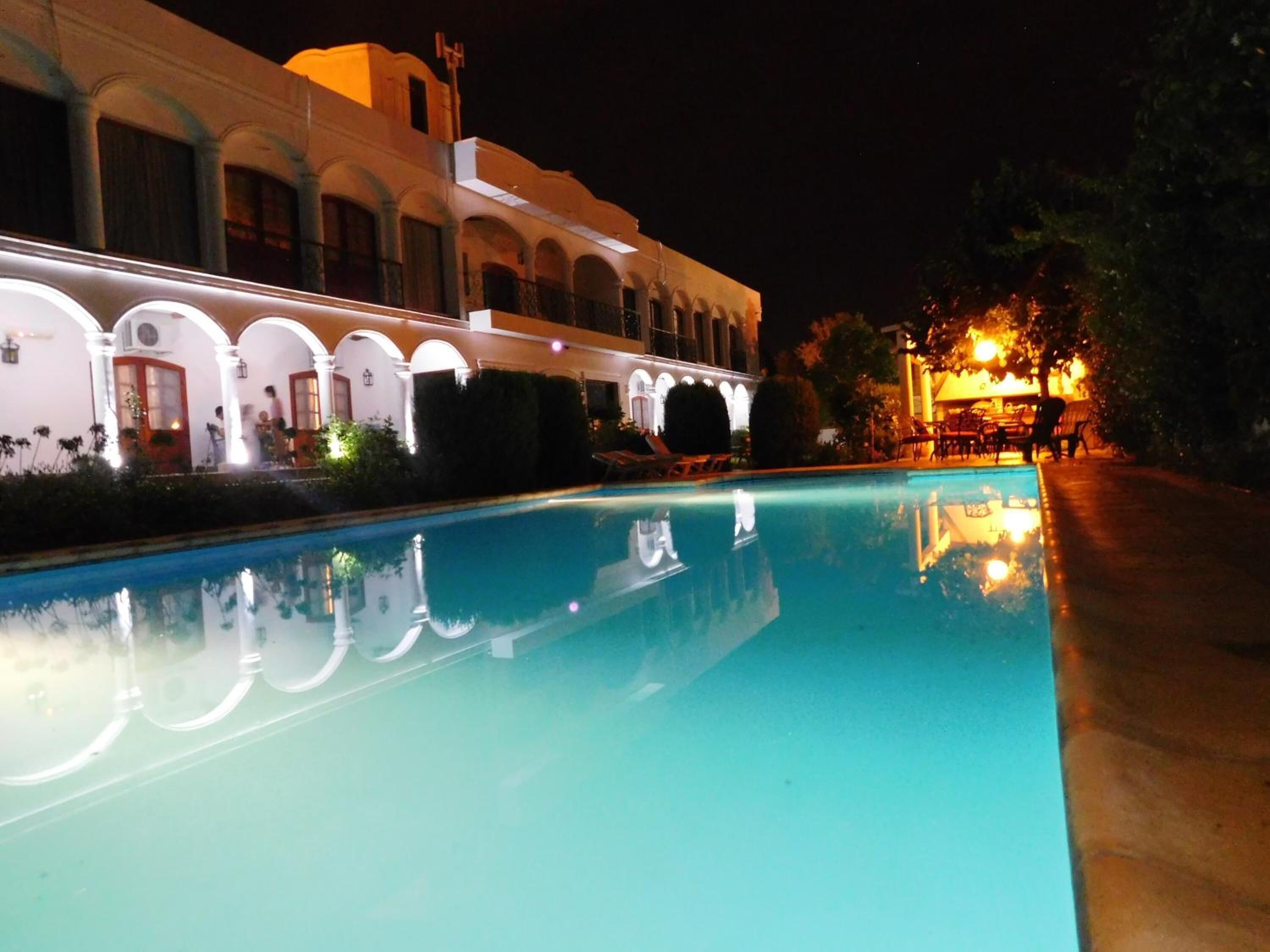 A swimming pool with a reflection of a building with arched windows and a warm-lit outdoor seating area.