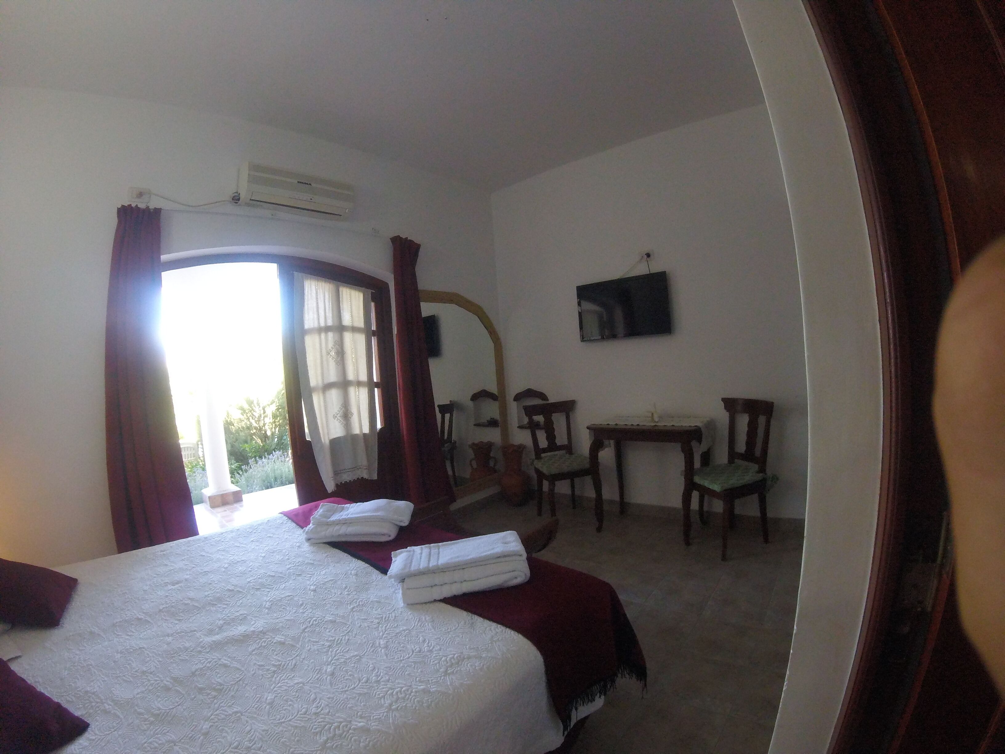 A hotel room with a bed, a desk, two chairs, a TV, and a window with curtains.