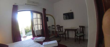 Una habitación de hotel con cama, escritorio, dos sillas, televisión y ventana con cortinas.