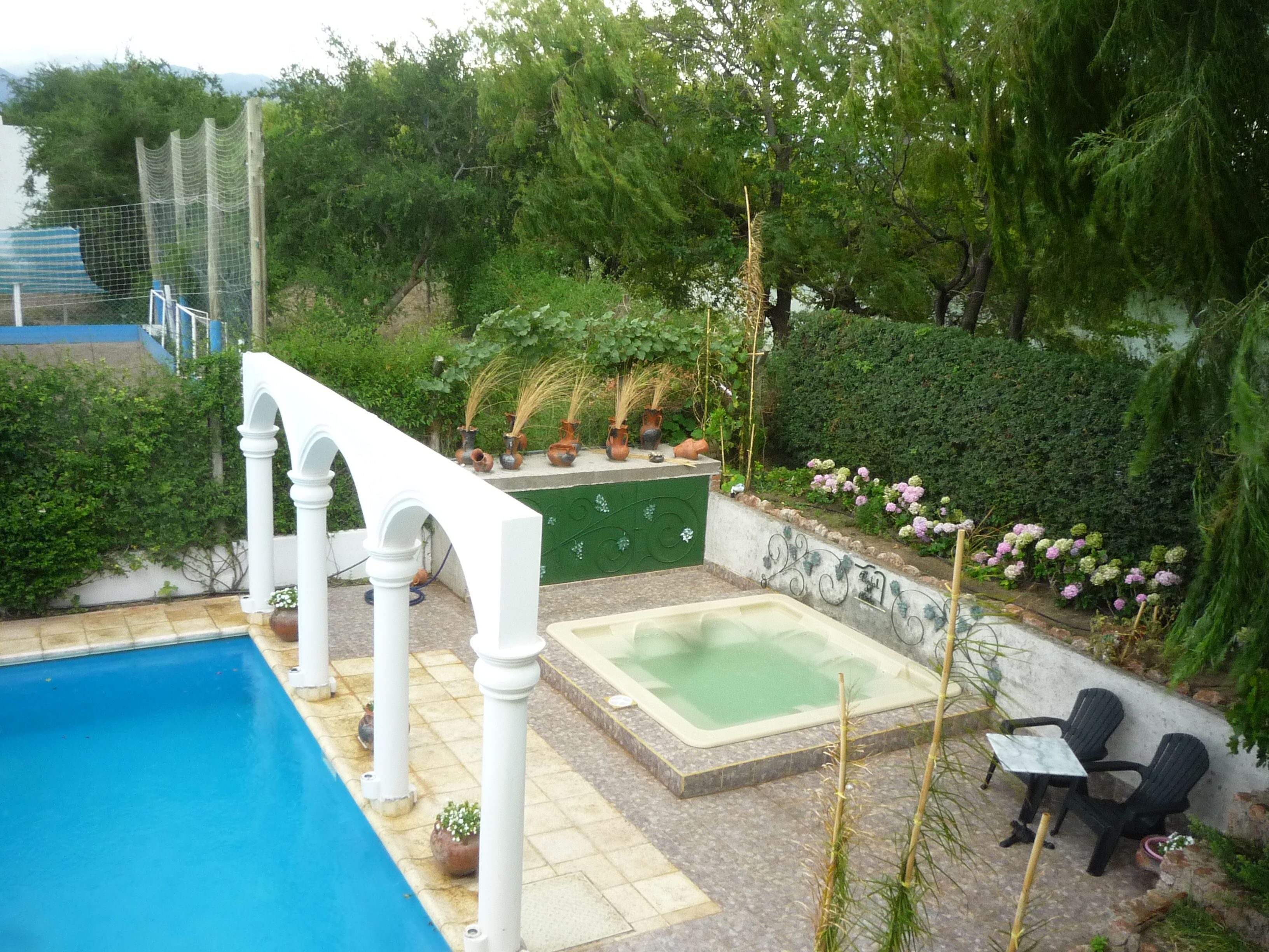 A swimming pool with a white pergola, a hot tub, and outdoor seating.
