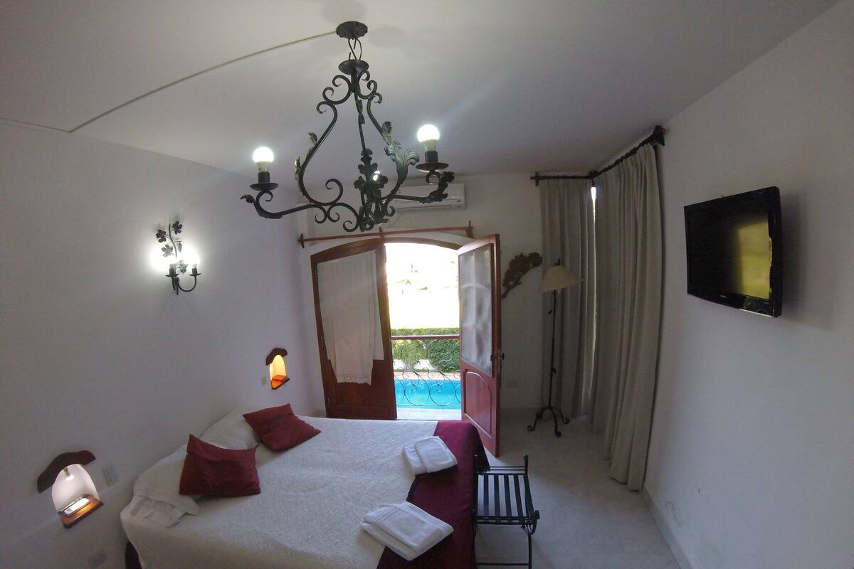 A bedroom with a large bed, a chandelier, a TV, and a view of a pool.