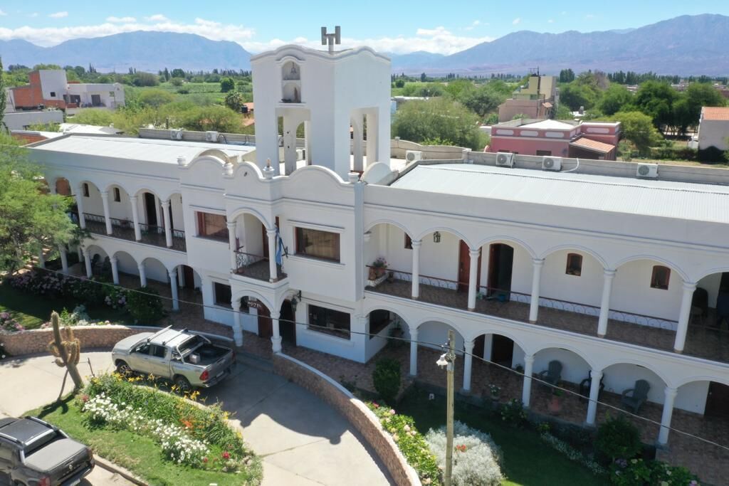 A white building with a central tower, multiple balconies, and a courtyard with a cactus and flowers.