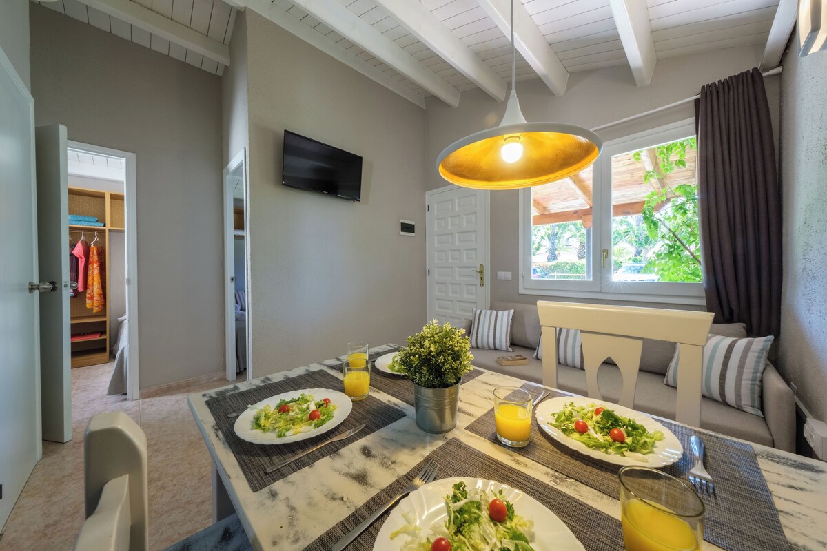 A dining area with a table set for four, a potted plant, and a TV mounted on the wall.