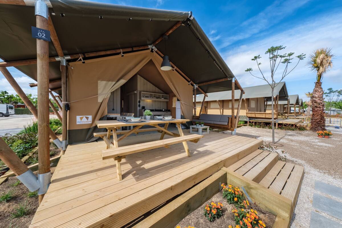 A tented outdoor area with a picnic table, wooden deck, and a small garden with flowers.