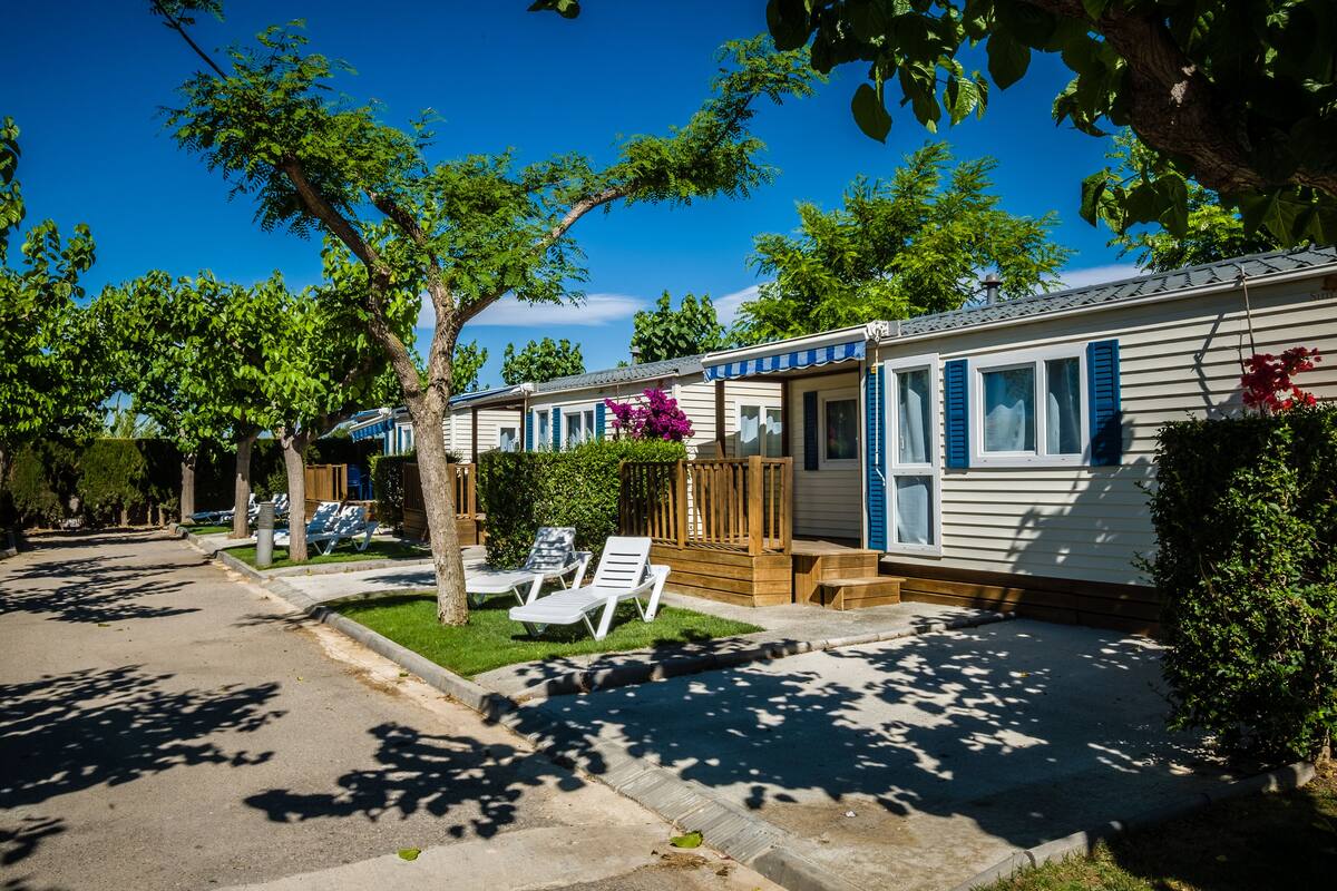A row of mobile homes with outdoor seating areas and a well-maintained lawn.