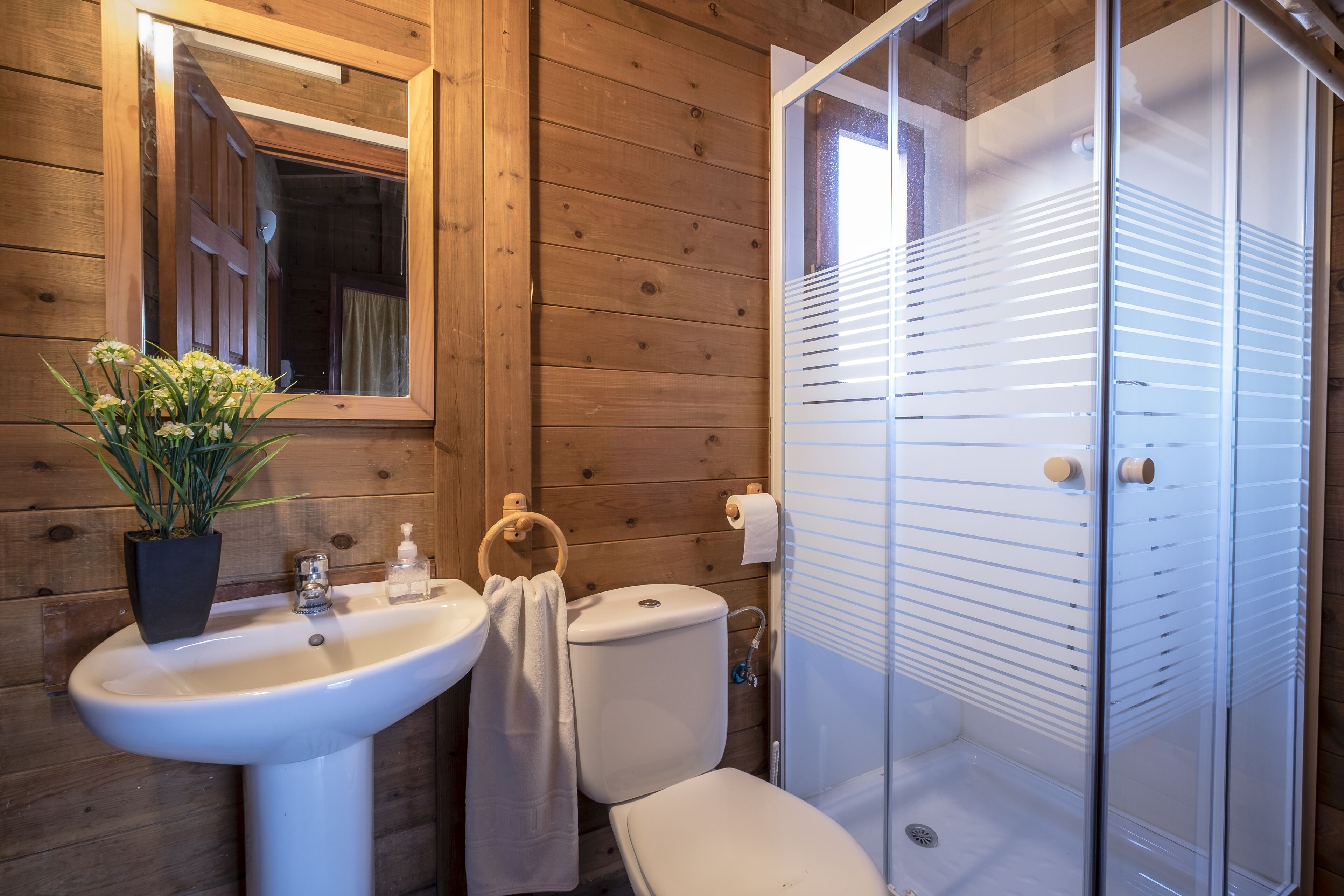 A wooden cabin bathroom with a sink, toilet, and shower.