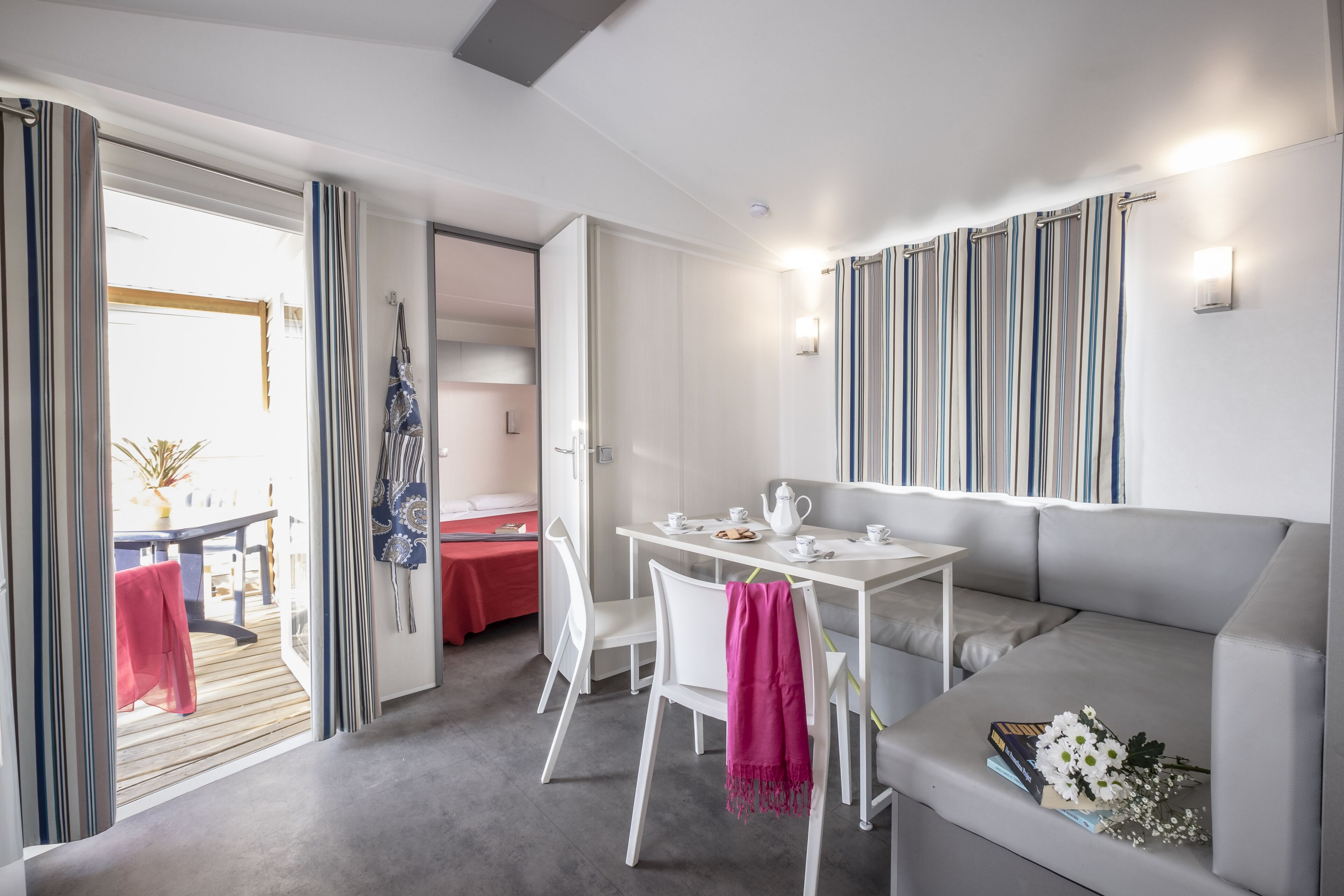 A modern room with a dining table, chairs, a sofa, and a balcony with curtains.