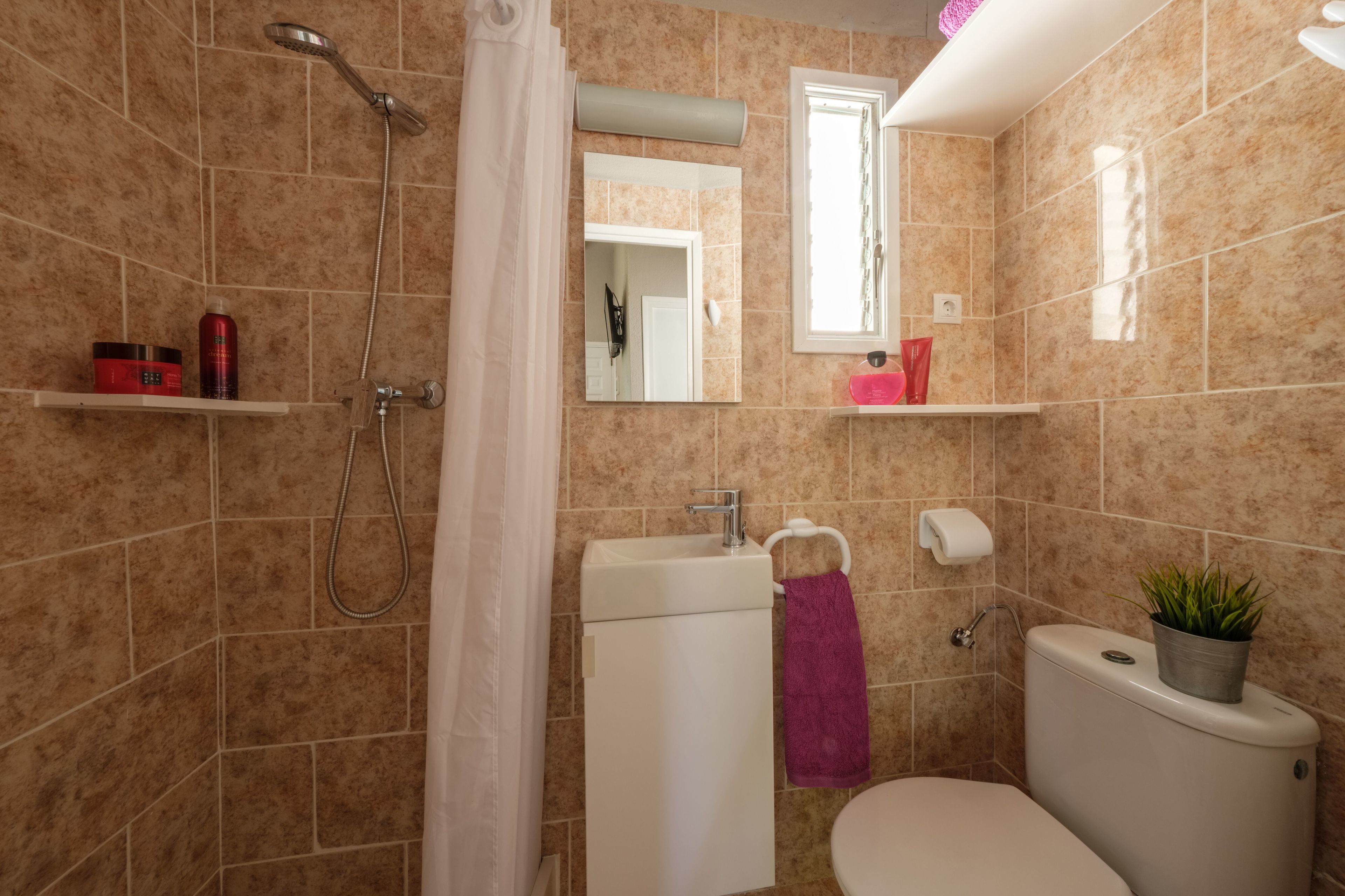 A bathroom with a shower, toilet, sink, and a mirror.
