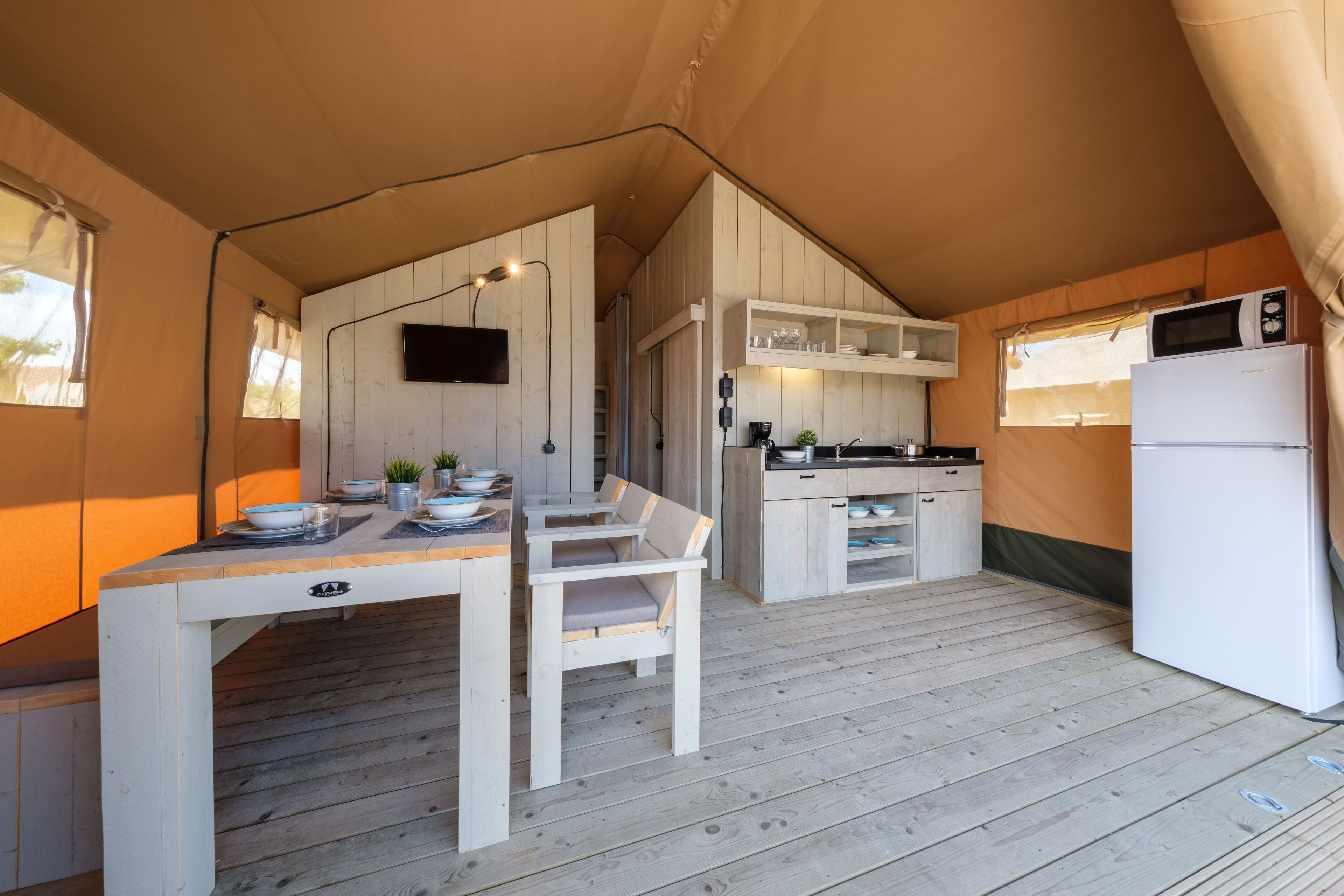 A tented accommodation with a dining area, kitchen, and a refrigerator.