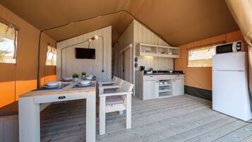 A tented accommodation with a dining area, kitchen, and a refrigerator.