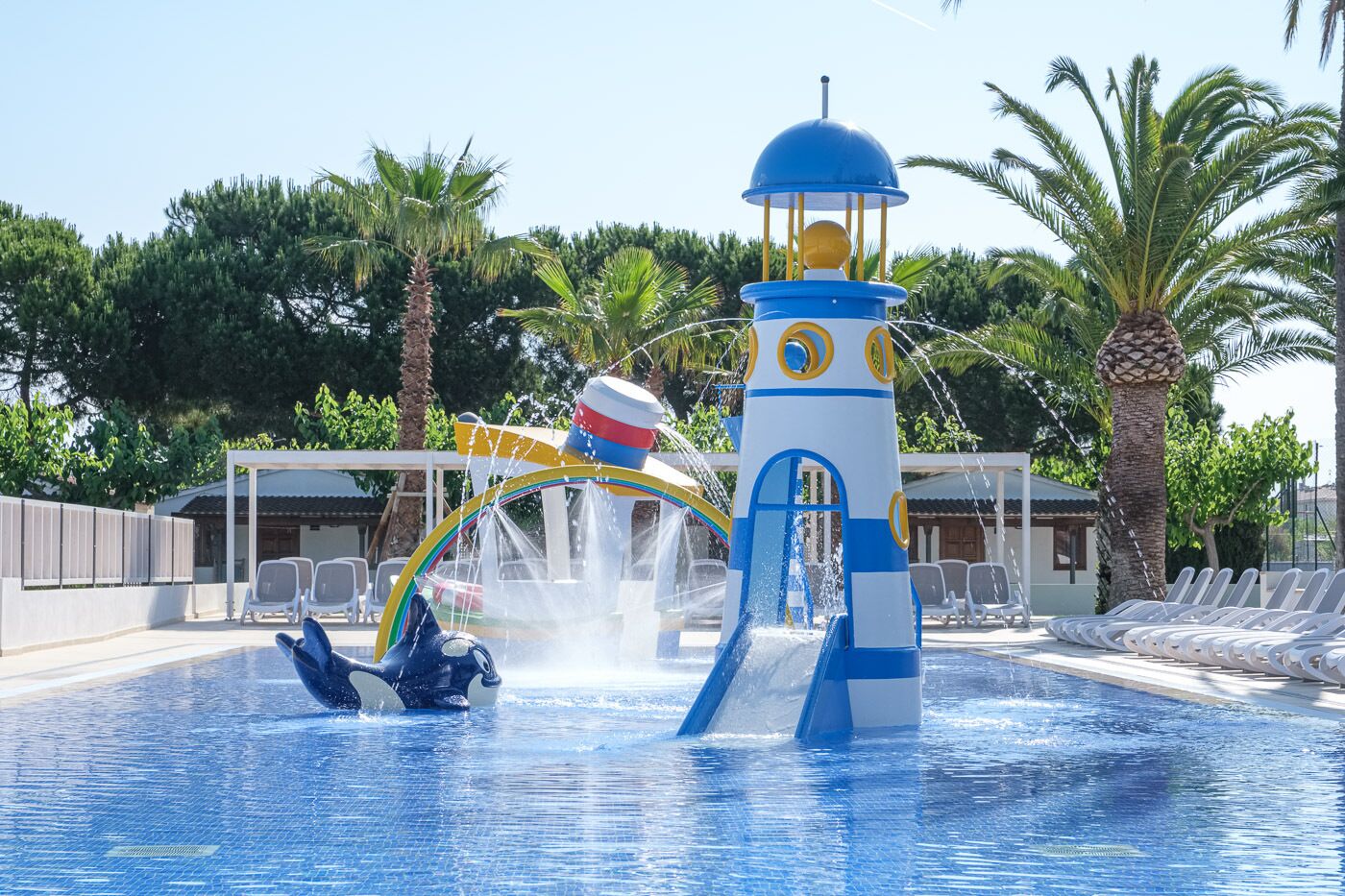A swimming pool with a water slide, lounge chairs, and palm trees.