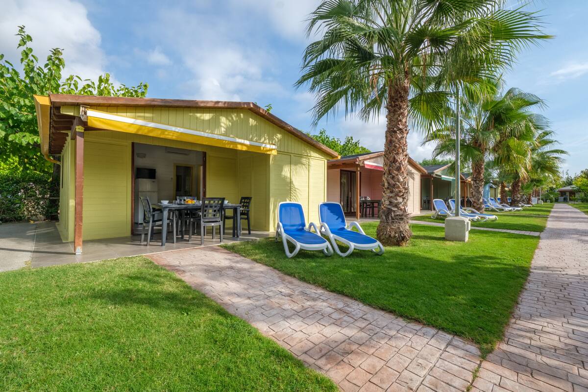 A covered outdoor area with a table and chairs, a paved walkway, and blue lounge chairs.