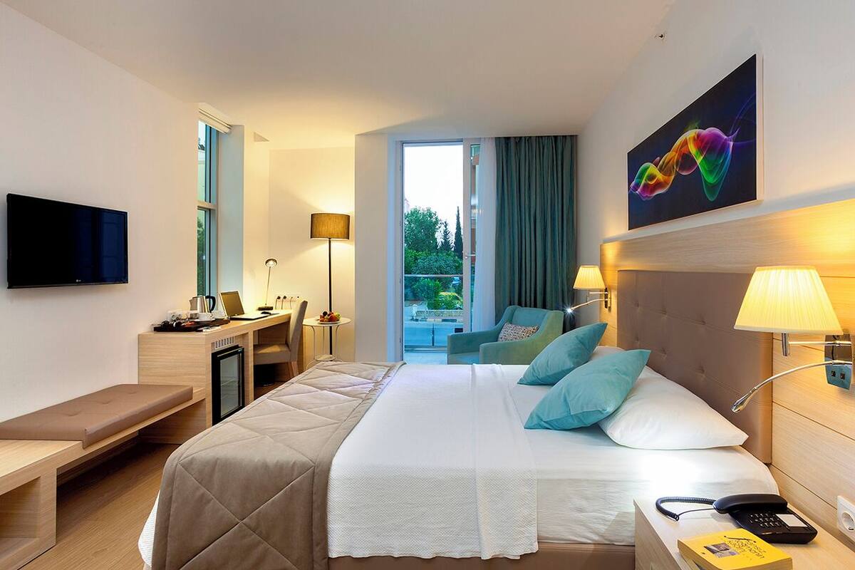 A hotel room with a bed, bedside table, desk, chair, lamp, and a TV.