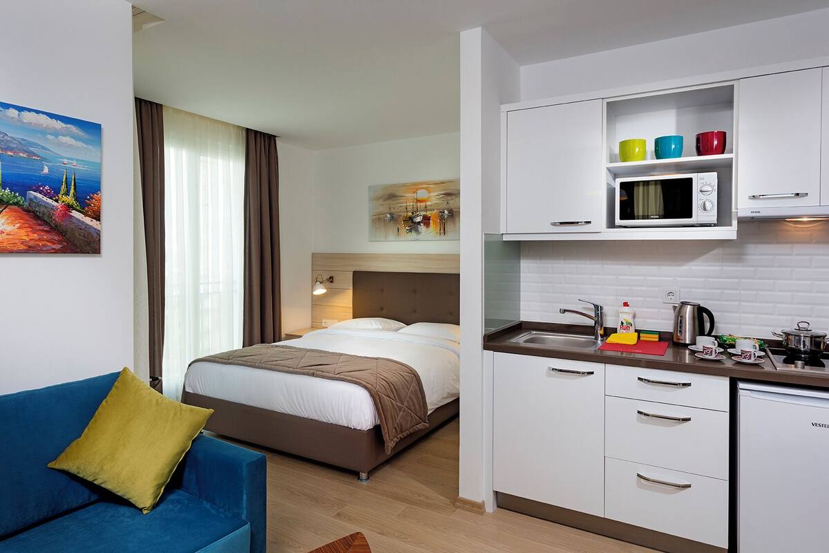 A hotel room with a bed, a blue sofa, a kitchenette with a microwave, and a painting on the wall.