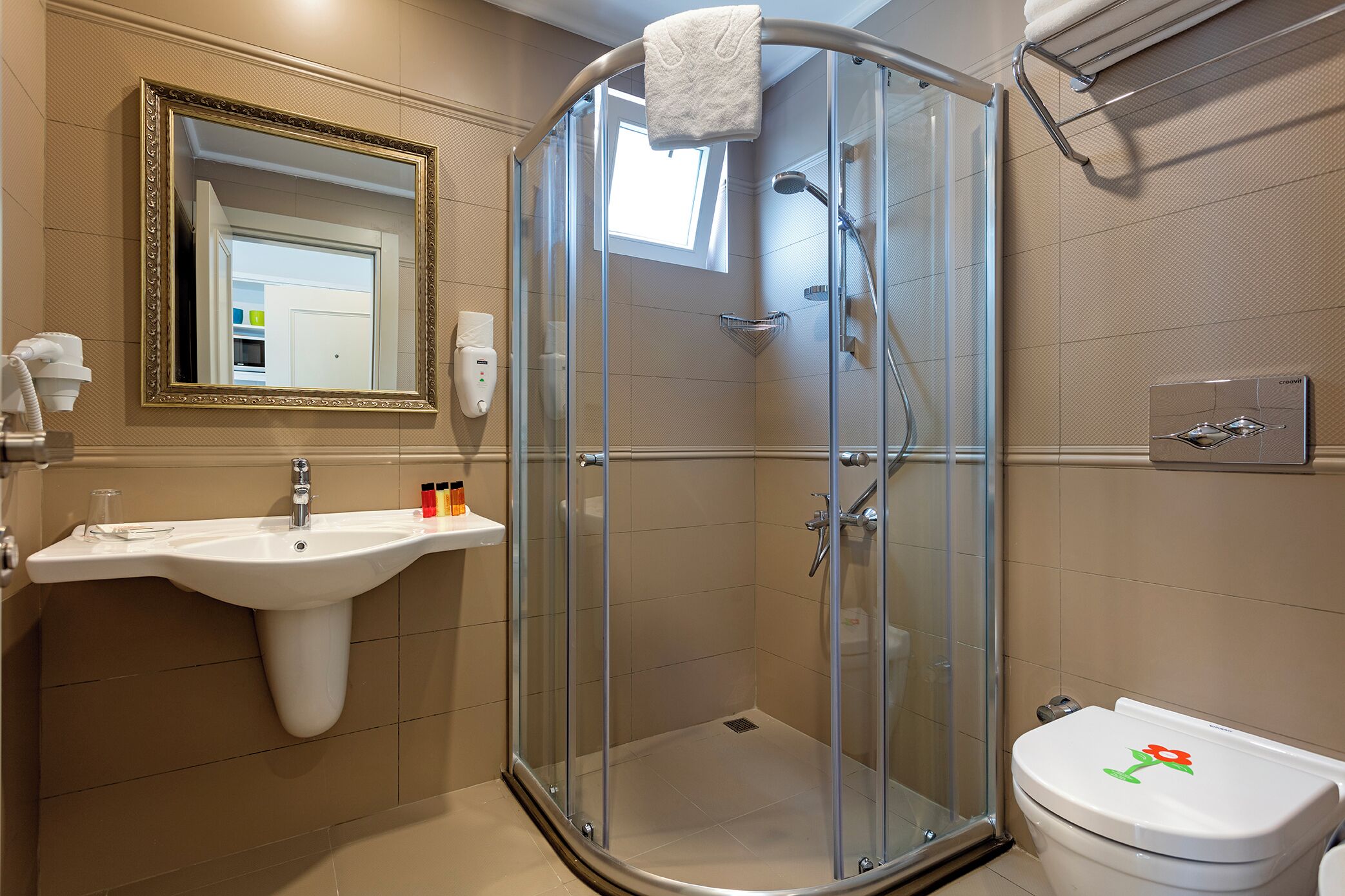 A bathroom with a glass shower enclosure, a sink, a toilet, and a mirror with a gold frame.