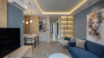 A modern living room with a flat-screen TV, a sofa, a coffee table, and a dining area with a table and chairs.